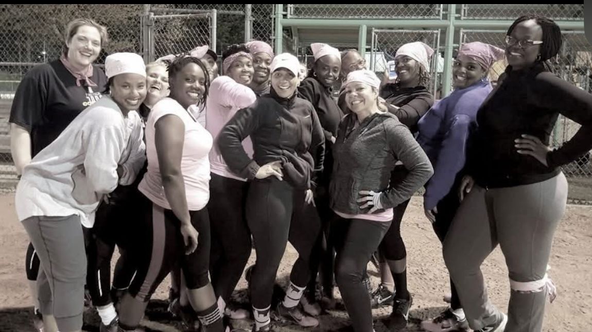 A team of women posing together on a softball field